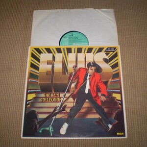 May include: A vinyl record album cover featuring Elvis Presley in a red jacket and black pants, standing on a stage with a microphone. The album title is "Elvis - The Sun Collection" and the record label is RCA.