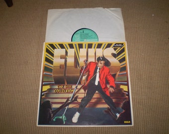 Può includere: Una copertina di un disco in vinile con Elvis Presley in giacca rossa e pantaloni neri, in piedi su un palco con un microfono. Il titolo dell'album è "Elvis - The Sun Collection" e l'etichetta discografica è RCA.