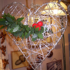 May include: A silver wire heart-shaped ornament decorated with green holly and red berries.