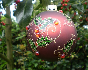 May include: A dark red Christmas ornament with a gold glitter finish and a green holly leaf design. The ornament has red and gold glitter accents.