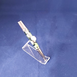May include: A silver pen with a green and white patterned barrel. The pen is on a clear acrylic stand.