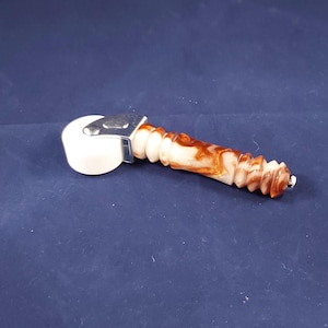 May include: A white and brown patterned seam roller with a metal bracket and a textured handle. The roller is designed for smoothing seams and edges in various craft projects. The handle is approximately 4 inches long.