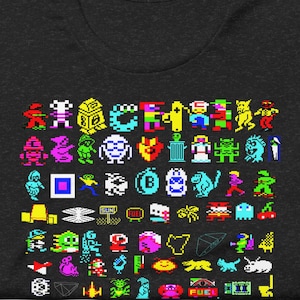 May include: Dark grey t-shirt with a colourful pixelated graphic of retro video game characters. The design features various shapes and colours, creating a nostalgic and playful aesthetic. The shirt is made of a soft material.