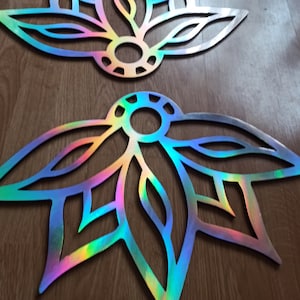 Puede incluir: Dos decoraciones de pared de flores de loto iridiscentes cortadas con láser. Las piezas decorativas tienen un diseño circular central con formas de pétalos que irradian hacia afuera. El color cambia de azul a verde y amarillo.