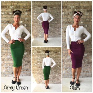 May include: Three women wearing white cardigans and different coloured skirts. The skirts are army green, plum, and burgundy. The women are standing in front of a brick wall.