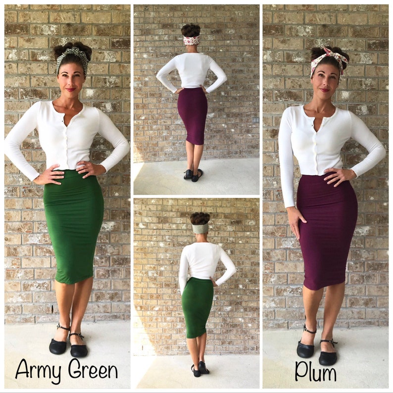 May include: Three women wearing white cardigans and different coloured skirts. The skirts are army green, plum, and burgundy. The women are standing in front of a brick wall.