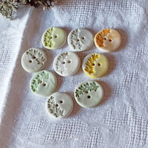 Peut inclure: Neuf boutons en céramique avec un motif de feuilles vertes. Les boutons sont dans différentes nuances de vert, jaune et orange.