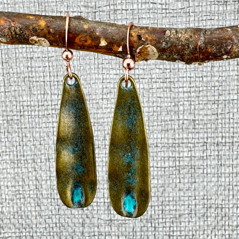 A pair of green earrings with blue accents hanging from a branch.