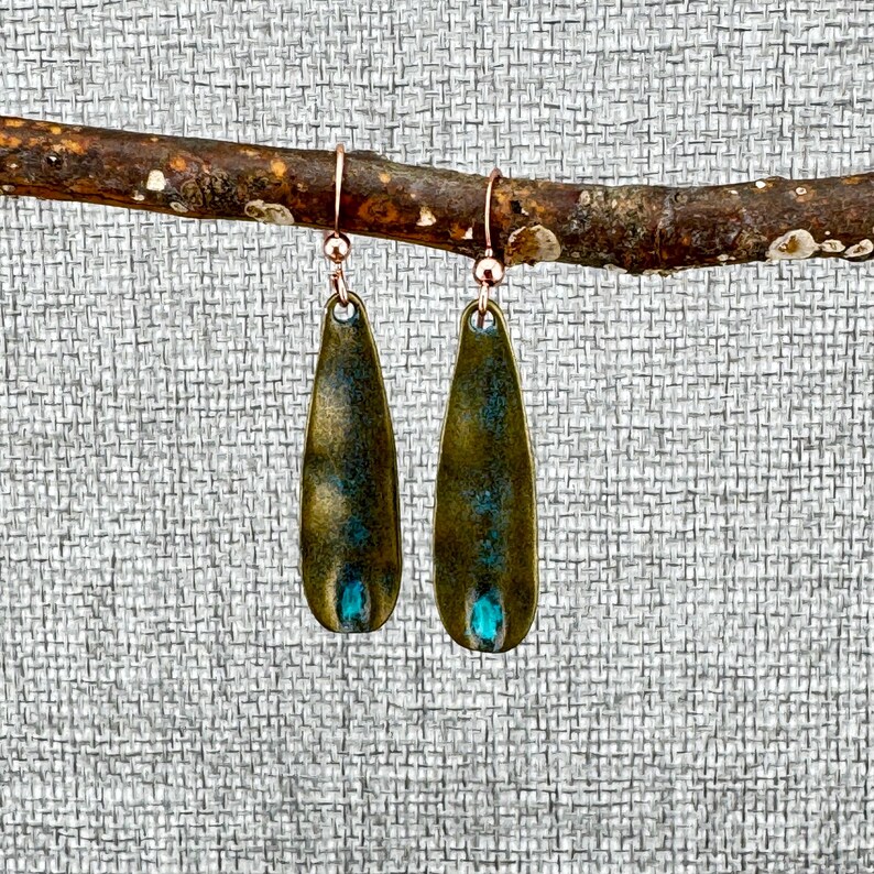 A pair of green earrings with blue accents hanging from a branch.