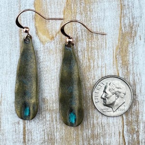 a pair of green earrings with a blue accent, placed next to a United States quarter.