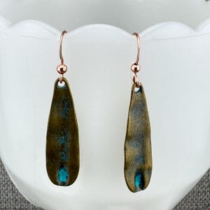 A pair of earrings with a dark green and blue color scheme, hanging from a white surface.