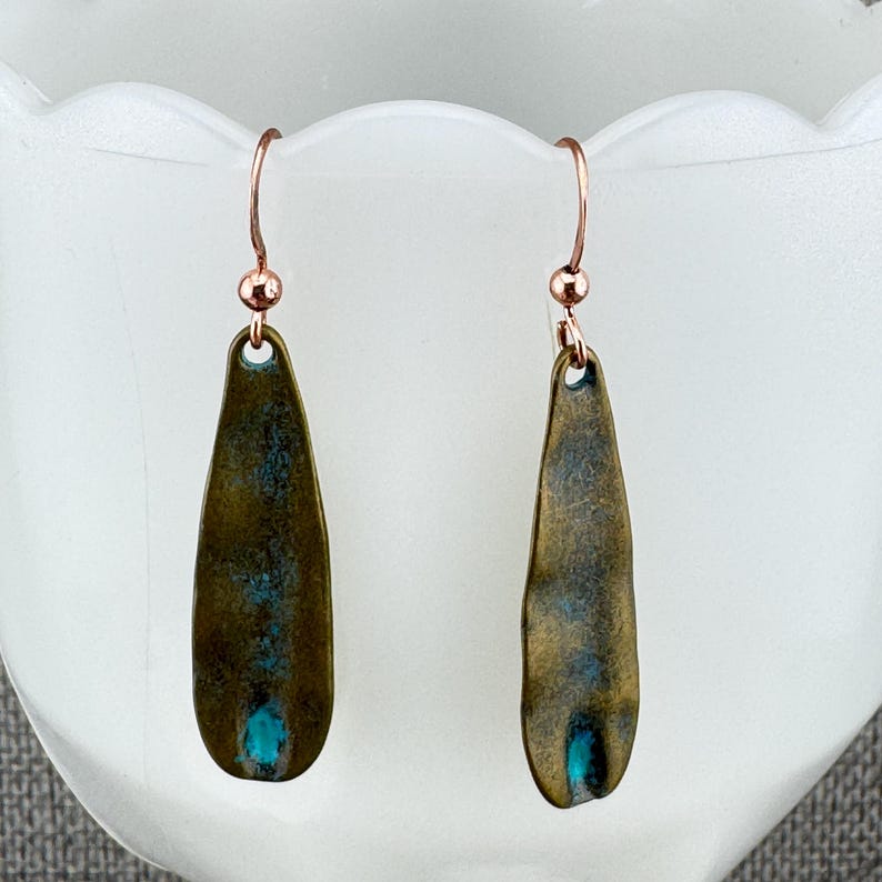 A pair of earrings with a dark green and blue color scheme, hanging from a white surface.