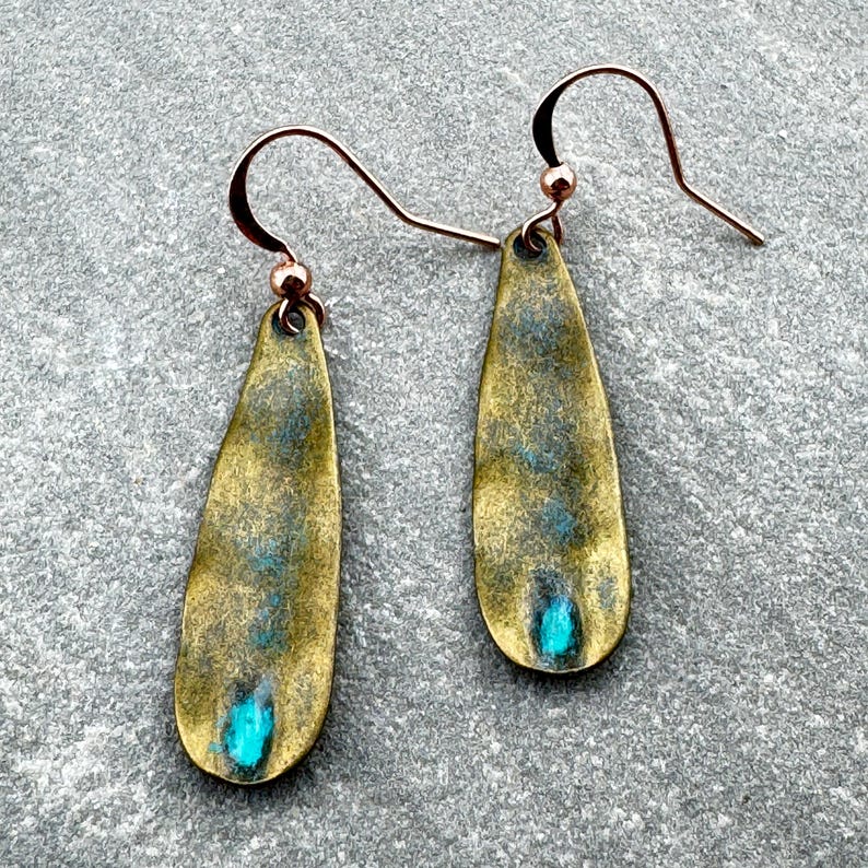 A pair of gold-colored earrings with blue accents, resting on a gray surface.