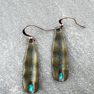 A pair of earrings with a greenish-blue stone in the center, resting on a gray surface.