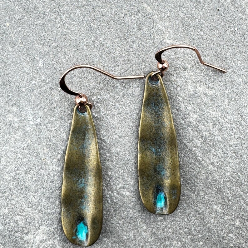 A pair of earrings with a greenish-blue stone in the center, resting on a gray surface.
