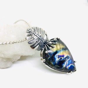 Puede incluir: Un collar de plata con un colgante de labradorita iridiscente en forma de lágrima y un dije de hoja de plata.
