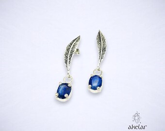 May include: A pair of silver earrings with blue gemstone drops and feather-shaped accents.
