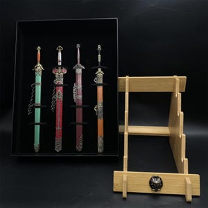 May include: A set of four miniature decorative swords in a black display case, each with a distinct colour scheme and detailed design. A separate bamboo sword stand is also included, with a decorative metal emblem.