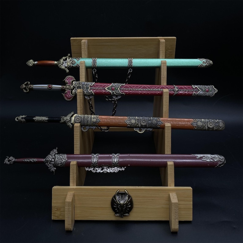May include: Four decorative swords on a wooden stand. The swords have ornate handles and sheaths in teal, red, brown, and burgundy. The stand is made of light-coloured wood and features a decorative emblem. The swords are displayed on a black background.