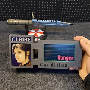 Peut inclure: Un couteau factice gris avec une lame argentée et un manche texturé, présenté avec une carte d'identité factice avec le nom "Claire" et le mot "Danger". La carte d'identité a une image pixélisée et le mot "Condition".