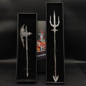 May include: Two decorative weapons in black display boxes. The weapon on the left is a silver axe with a twisted handle. The weapon on the right is a silver trident with a twisted handle. Both weapons have a black background and the word "MYSTERY" is printed on the box on the right.