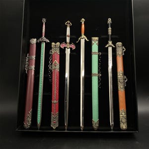 May include: A collection of six decorative swords with detailed hilts and sheaths. The swords have silver blades and sheaths in red, green, and brown. The hilts are intricately designed. The swords are displayed in a black case.