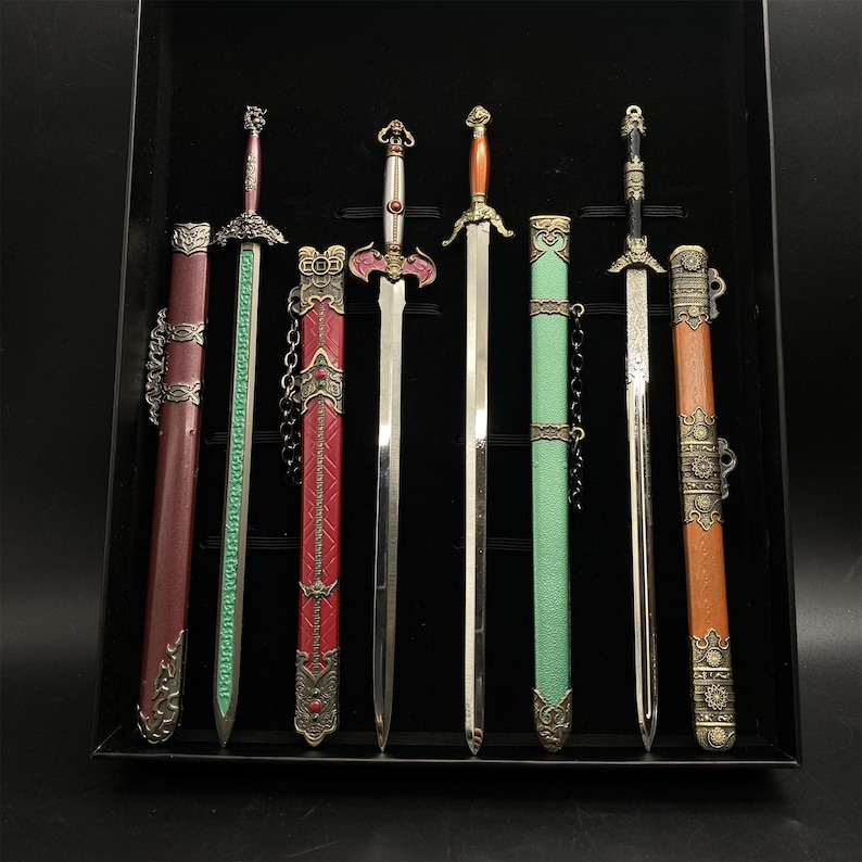 May include: A collection of six decorative swords with detailed hilts and sheaths. The swords have silver blades and sheaths in red, green, and brown. The hilts are intricately designed. The swords are displayed in a black case.