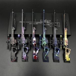Puede incluir: Seis modelos de rifles de francotirador en miniatura dispuestos en fila, cada uno con un patrón gráfico colorido único en la culata y el cañón. La colección incluye diseños con calaveras, serpientes y motivos abstractos, todos con miras telescópicas.