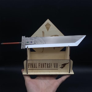 May include: A silver-colored sword with a wooden handle and a red and brown hilt. The sword is resting on a wooden stand with the words "FINAL FANTASY VII" engraved on the front.