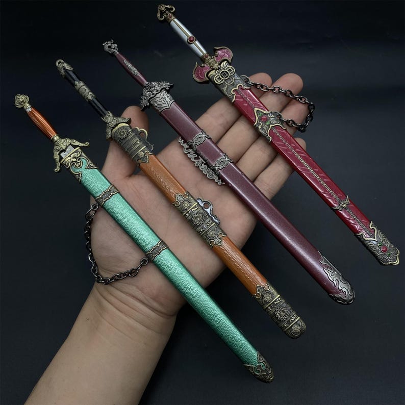 May include: Four miniature decorative swords with detailed handles and sheaths. The swords are in shades of red, brown, green, and bronze. Each sword has a chain attached to the sheath. The swords are presented against a dark backdrop.