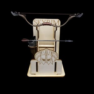 May include: A wooden display stand featuring a bow, arrow, and a small container. The stand has the word "SKYRIM" engraved on it, along with a decorative helmet design. The bow is metallic with a brown grip.