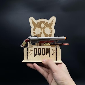 May include: A wooden stand featuring a Doom logo and a demon skull design. A miniature silver and red shotgun is displayed on the stand.