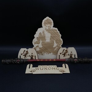 May include: A wooden stand with a laser-engraved image of a monkey holding a staff. The stand has the words "Black Myth Wukong" engraved on it. The stand is designed to hold a staff or other similar object.