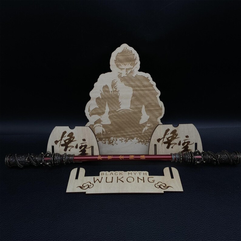 May include: A wooden stand with a laser-engraved image of a monkey holding a staff. The stand has the words "Black Myth Wukong" engraved on it. The stand is designed to hold a staff or other similar object.