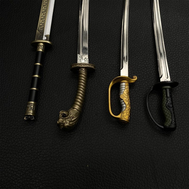 May include: Four decorative miniature swords with ornate handles and silver blades are displayed against a black background. The handles feature various designs, including a lion's head, gold accents, and black and gold detailing. The blades are sharp and reflective.