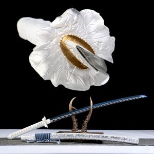 May include: A decorative katana sword with a white handle and scabbard, and a blue blade. The sword is displayed on a wooden stand with a white floral design and gold accents. The blade is approximately 30 inches long.