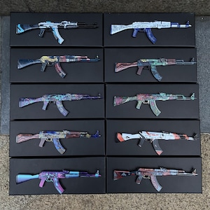 Op de afbeelding: Een assortiment AK-47-stijl geweren met diverse kleurrijke ontwerpen. Elk geweer wordt gepresenteerd op een zwart oppervlak. De geweren hebben een reeks patronen, waaronder blauw, paars, rood en groen, met ingewikkelde details op de kolven en lopen.