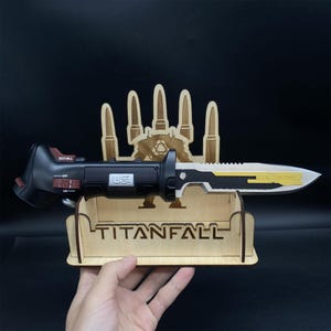 May include: A black and gold Titanfall knife with a wooden stand. The stand features a silhouette of a Titan and the word "Titanfall".