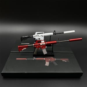 Pode incluir: Três rifles de brinquedo vermelhos, brancos e pretos, exibidos em uma superfície preta. O rifle vermelho está no centro, com um carregador prateado e uma extensão de cano vermelha. O rifle branco está no topo e o rifle preto na parte inferior.