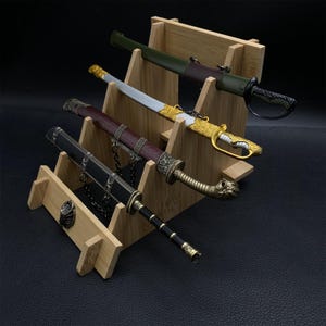 May include: Four decorative swords displayed on a bamboo stand. The swords feature ornate handles and sheaths in various colors, including black, gold, green, and brown. The stand has multiple levels to showcase the swords.