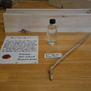 May include: A handwritten letter with a red wax seal, a small glass bottle with a black cap, a wooden stick, and a handwritten tag that reads "19 1/2" Oak and Pixie Dust".