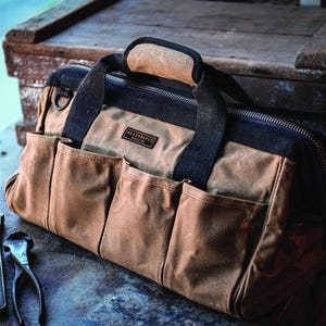May include: A brown canvas tool bag with multiple exterior pockets and a black zipper. The bag has a tan handle and a black strap. The label reads "READTWARES SUPPLY CO."