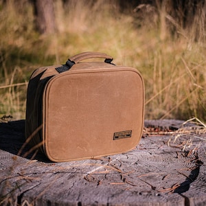 May include: A brown canvas travel bag with a black handle and a black label that says "Field Notes" on it.