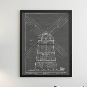 以下が含まれることがあります： 黒い額縁に入ったヴィンテージな風車の設計図のプリントが、白いクッションのある濃い青色のソファの上に飾られています。手前に、幾何学的なシェードの黒い三脚のフロアランプと、本と鉢植えの植物が置かれたサイドテーブルがあります。