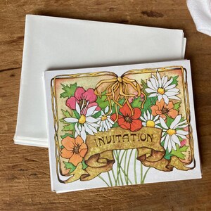 May include: A white card with a gold border and a floral design. The card has the word "Invitation" printed on it.