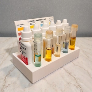 May include: A white tray contains a saltwater master test kit with bottles, test tubes, and a pH colour chart. The kit's text reads "SALTWATER MASTER TEST KIT" and "HIGH RANGE pH". The test tubes contain various coloured liquids.