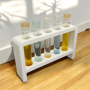 May include: A white test tube rack with six clear glass test tubes filled with different coloured liquids. The liquids are yellow, blue, green, and clear.