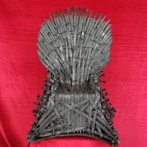 May include: A black metal replica of the Iron Throne from the Game of Thrones television series. The throne is made of swords and has a seat made of metal.