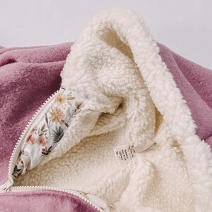 May include: A mauve hooded jacket with a white sherpa lining and a floral print on the inside of the hood. The tag reads "Made in USA, 100% Wool, Size 12M".