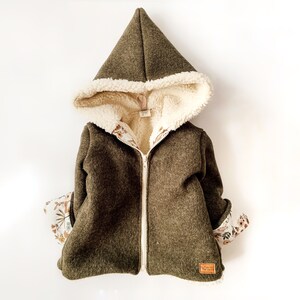 May include: A green hooded jacket with a white sherpa lining and floral print lining. The jacket has a zipper closure and a brown leather label.